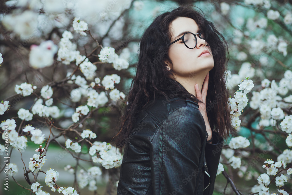Outdoor spring portrait of fashion sensual young girl posing in amazing blooming garden. Wearing a hat and leather jacket, feminine look, elegant glamorous style. On the background of cherry blossoms Outdoor spring portrait of fashion sensual young girl posing in amazing blooming garden. Wearing a hat and leather jacket, feminine look, elegant glamorous style. On the background of cherry blossoms
