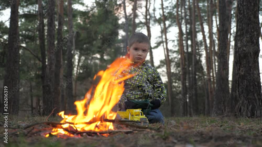 Sad child sitting near the fire in the park, forest. Kid sitting alone near the fire-raising. Boy thinking about his problems while sitting near the fireplace. Child of refugee kneeling near the fire Sad child sitting near the fire in the park, forest. Kid sitting alone near the fire-raising. Boy thinking about his problems while sitting near the fireplace. Child of refugee kneeling near the fire