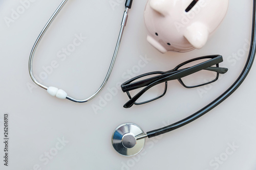 Medicine doctor equipment stethoscope or phonendoscope piggy bank glasses isolated on white background. Health care financial checkup or saving for medical insurance costs concept