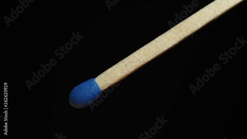 Extreme closeup of blue matchstick igniting, burning and fuming in slowmotion on black background