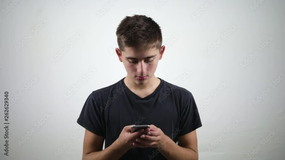 An attractive young man uses a phone and smiles against a white background. Medium shot An attractive young man uses a phone and smiles against a white background. Medium shot