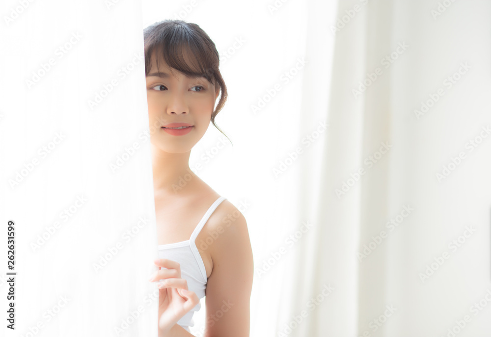 Portrait of beautiful young asian woman standing at the window and smile while wake up with sunlight at morning, girl happy with fresh and cheerful, lifestyle and relax for wellness concept. Portrait of beautiful young asian woman standing at the window and smile while wake up with sunlight at morning, girl happy with fresh and cheerful, lifestyle and relax for wellness concept.