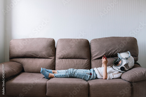 Adorable little girl sitting on couch. He is lying on couch while playing with a video game console at home