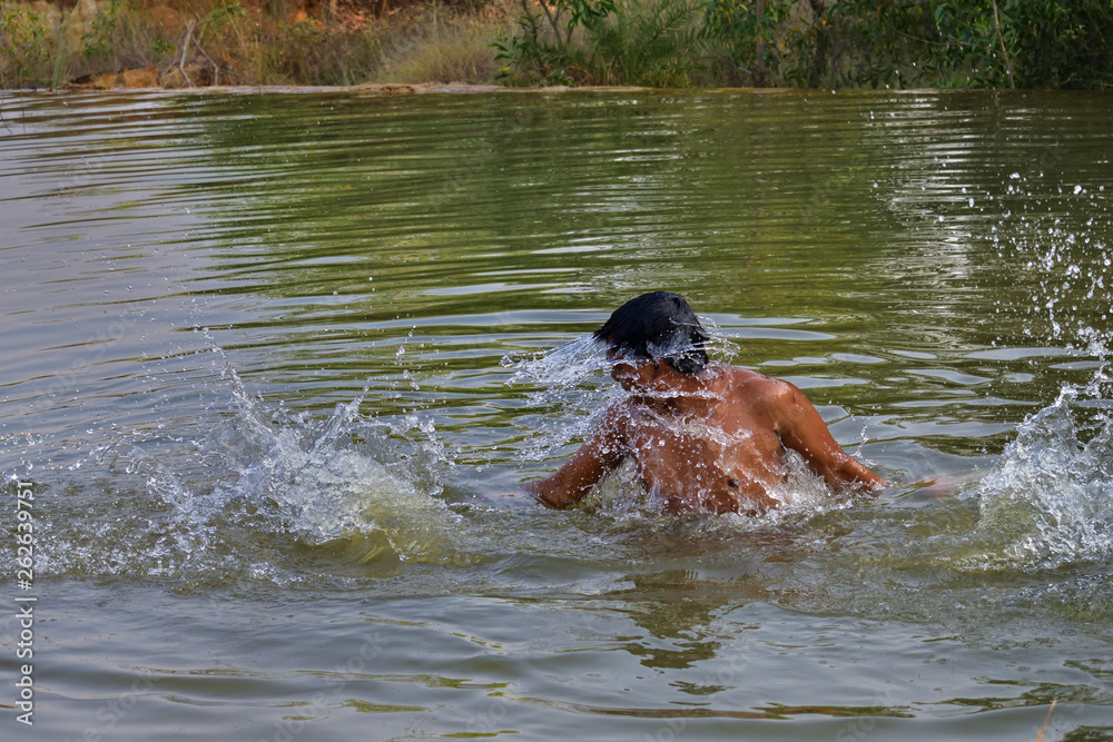 young man swimming in the pond or pool on a summer noon . Summer swimming. playing with water in summer season