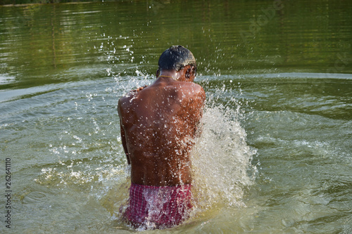 Fototapeta Naklejka Na Ścianę i Meble -  A man bathing in a natural lake, refreshing himself from heat of summer in summer season in rural India, at Nature Reserve.