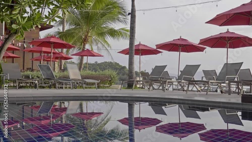 Beautiful Hotel Pool Scenery With Red Umbrellas Beds Calm Water and Tropical Vegetation in Background 4k photo