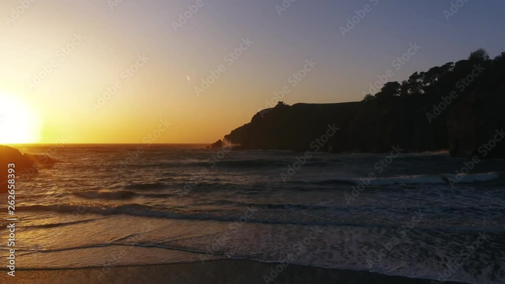 Drone captures a setting sun at golden hour over a lonely cove with a rocky beach. Haze and setting sun create a dreamy and surreal vibe. Drone captures a setting sun at golden hour over a lonely cove with a rocky beach. Haze and setting sun create a dreamy and surreal vibe.