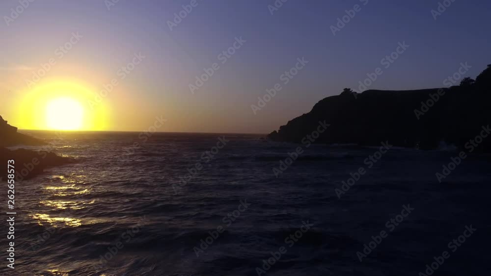 Drone captures a setting sun at golden hour over a lonely cove with a rocky beach. Haze and setting sun create a dreamy and surreal vibe. Drone captures a setting sun at golden hour over a lonely cove with a rocky beach. Haze and setting sun create a dreamy and surreal vibe.