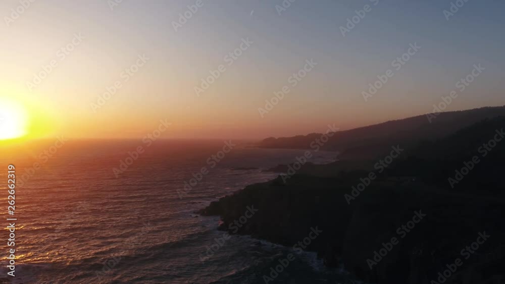 Drone captures a setting sun at golden hour over a lonely cove with a rocky beach. Haze and setting sun create a dreamy and surreal vibe. Drone captures a setting sun at golden hour over a lonely cove with a rocky beach. Haze and setting sun create a dreamy and surreal vibe.