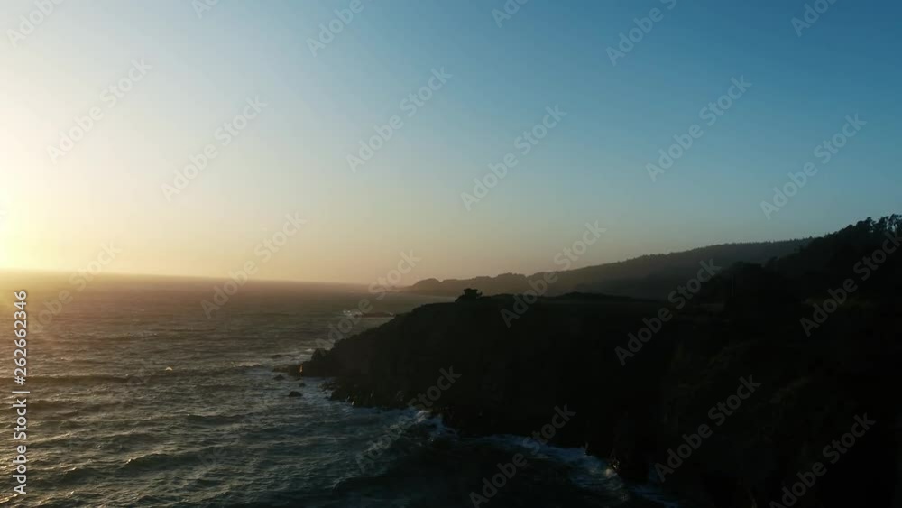 Drone captures a setting sun at golden hour over a lonely cove with a rocky beach. Haze and setting sun create a dreamy and surreal vibe. Drone captures a setting sun at golden hour over a lonely cove with a rocky beach. Haze and setting sun create a dreamy and surreal vibe.