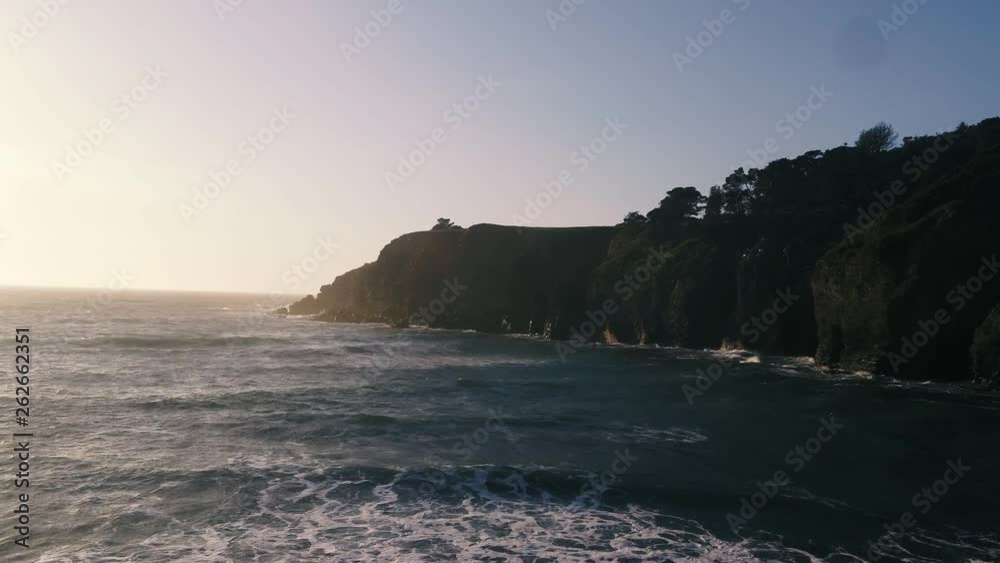 Drone captures a setting sun at golden hour over a lonely cove with a rocky beach. Haze and setting sun create a dreamy and surreal vibe. Drone captures a setting sun at golden hour over a lonely cove with a rocky beach. Haze and setting sun create a dreamy and surreal vibe.