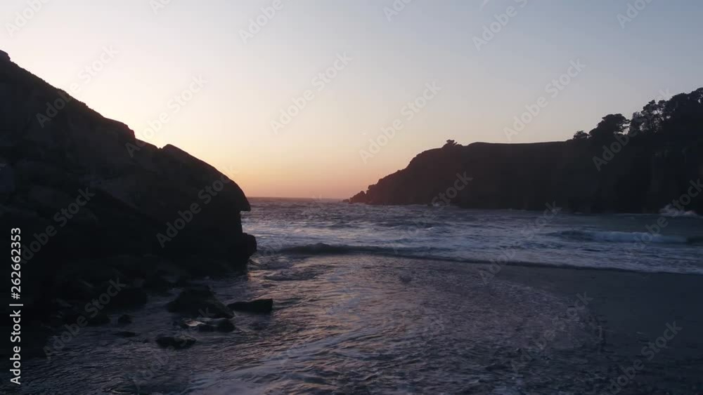 Drone captures a setting sun at golden hour over a lonely cove with a rocky beach. Haze and setting sun create a dreamy and surreal vibe. Drone captures a setting sun at golden hour over a lonely cove with a rocky beach. Haze and setting sun create a dreamy and surreal vibe.