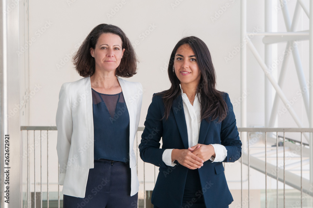 Two smiling business woman posing at camera in office hall Two smiling business woman posing at camera in office hall