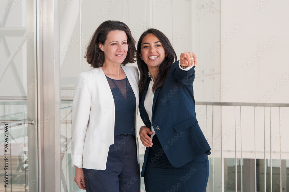 Two smiling business women pointing away in office hall Two smiling business women pointing away in office hall