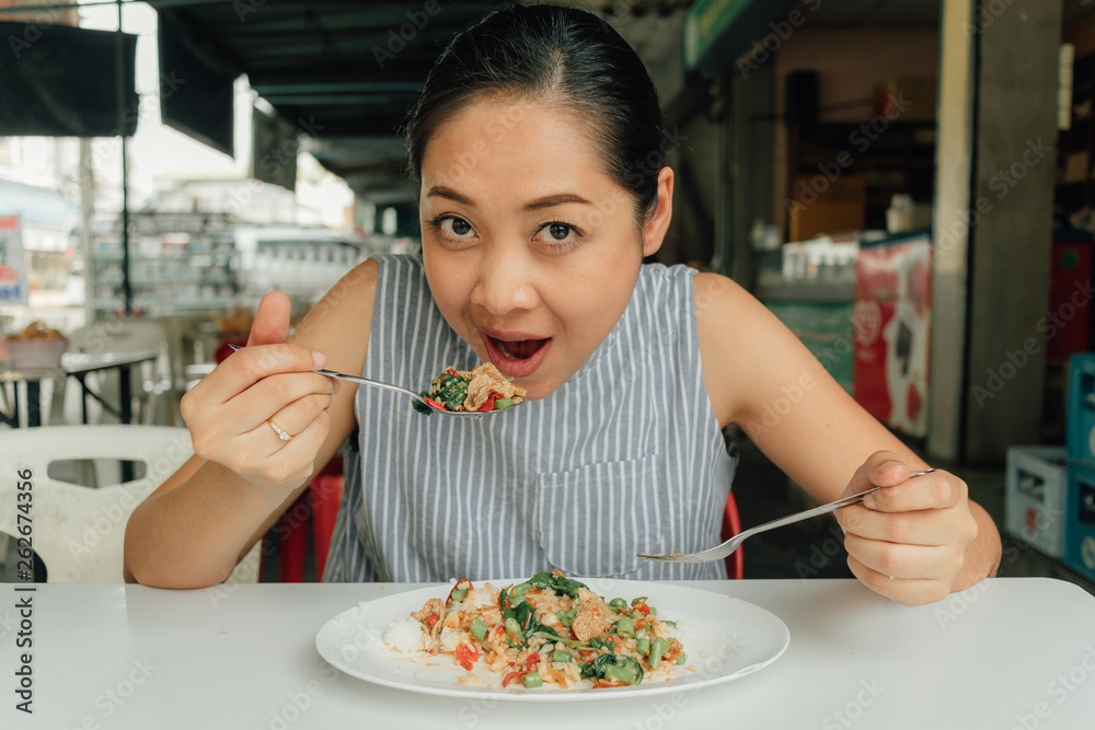 Woman is eating Thai rice stir-fried pork and basil.