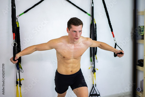 A young man stretches TRX simulators to maintain to the beautiful shape of his body. A healthy generation of young guys.