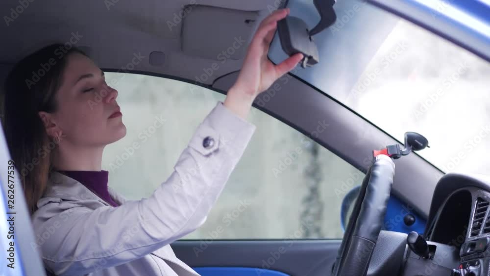Beautiful young successful woman looks in the car mirror while sitting behind the wheel and getting ready for the trip
