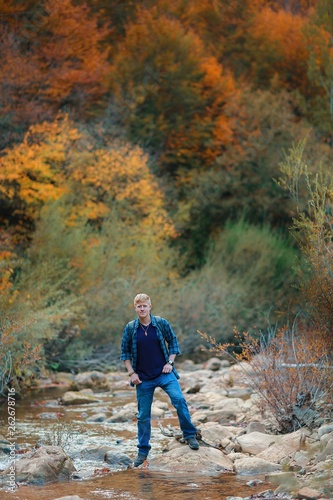 Redhead man in a plaid shirt and purple t-shirt stands on the stones in the mountain stream in the autumn forest in the Grand Canyon of Crimea. Autumn, travel and hiking concept. © Андрей Рыков