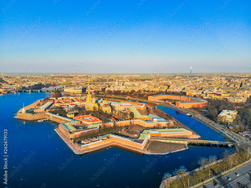 Fototapeta premium Beautifull aerial view of the Petropavlovsky fortress in sunny spring day. Golden tall spire of famous Peter and Paul Cathedral on the blue sky background. Historical centre of St. Petersburg, Russia.