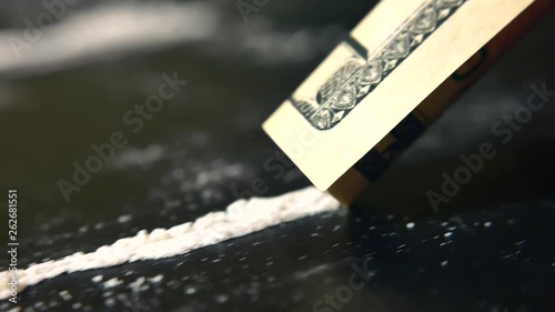 Addict sniffs  line of cocaine through a rolled dollar bill from a black table in room, close-up, macro. Drug abuse. Drug use, addiction, social issues. Illegal substances and dirty money. 4K