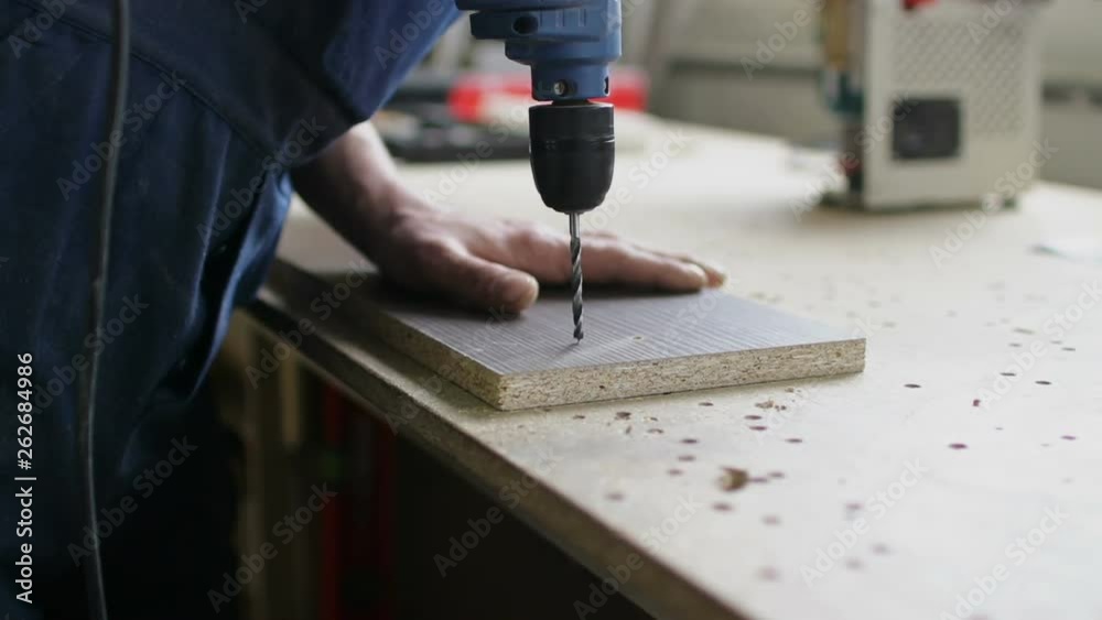 Man hands make holes in wooden board with electric drill Man hands make holes in wooden board with electric drill