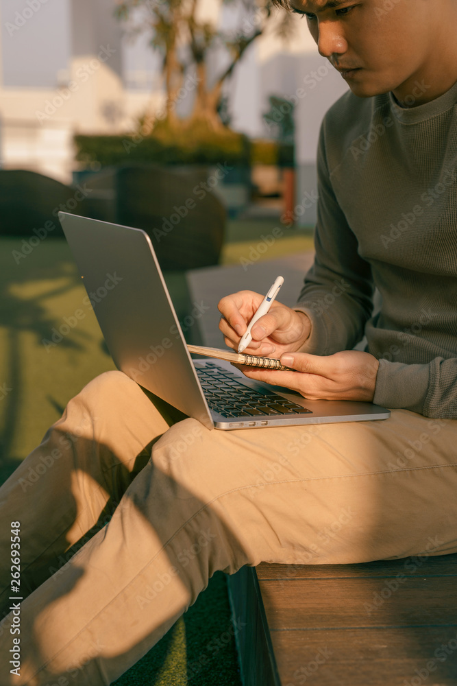 a businessman sitting with the laptop on his knees and writing the notebook a businessman sitting with the laptop on his knees and writing the notebook
