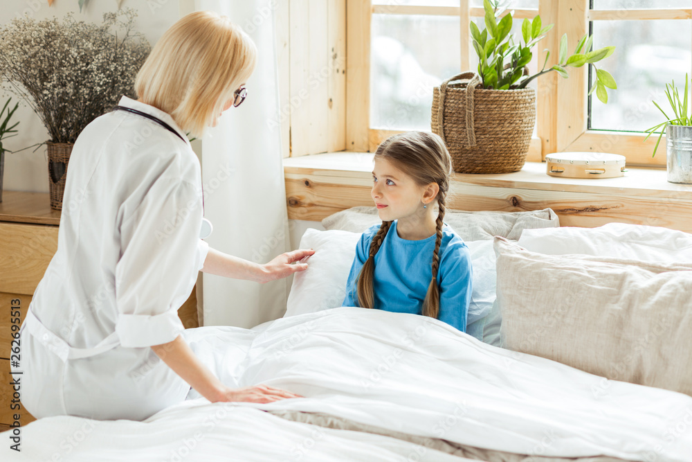 Charming pediatrician putting small sick girl to a bed Charming pediatrician putting small sick girl to a bed