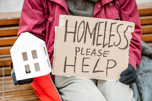 Homeless beggar holding paper house and message for help on a cardboard begging and grieving for a shelter for living