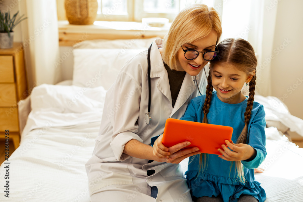 Pleasing physician looking at a tablet with a small girl. Pleasing physician looking at a tablet with a small girl.
