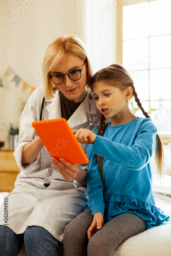Sweet girl pointing at tablet while doctor looking at it.