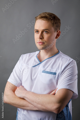 Medical staff. Young sympathetic doctor stands isolated on a grey background dressed in a uniform for doctors © nazariykarkhut
