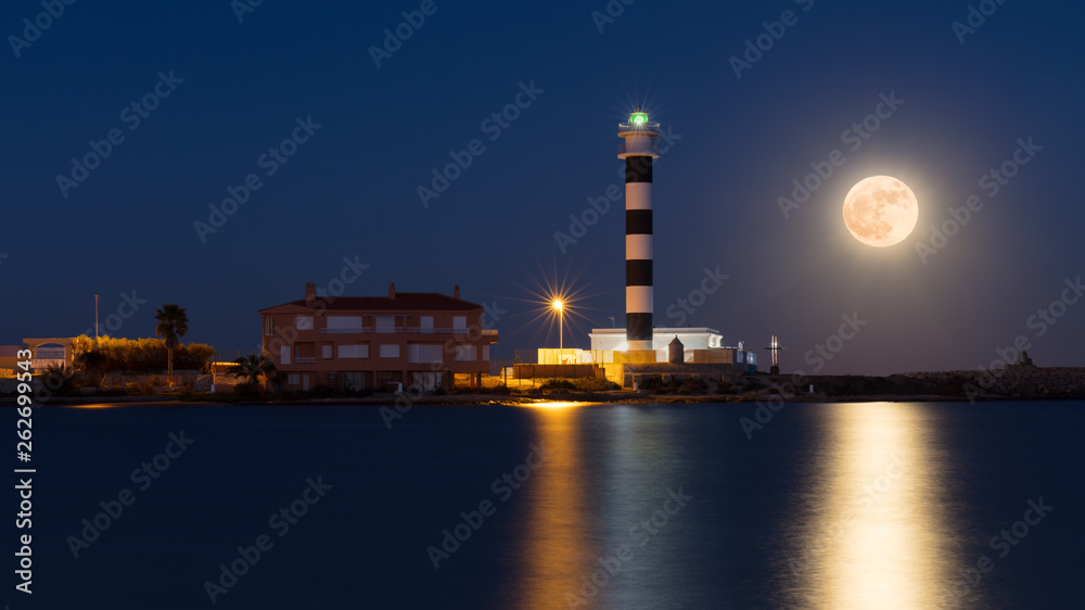 A blue and white lighthouse on the Mar Menor, the Faro del Estacio, on rising full moon on a warm summer night