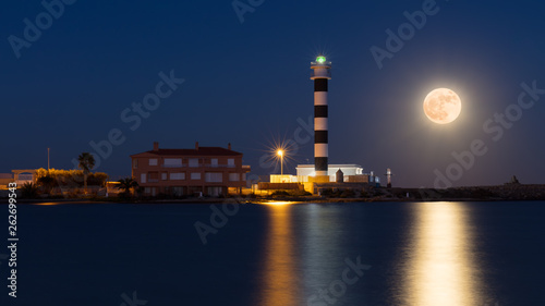 A blue and white lighthouse on the Mar Menor, the Faro del Estacio, on rising full moon on a warm summer night