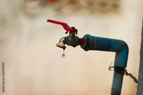 Slow water drop from a leaking on an old rusty water tap - water shortage - save water concept