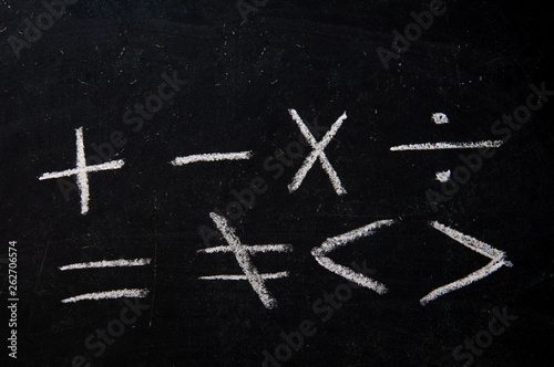 Arithmetic signs in white chalk on a black chalkboard.