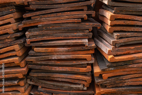 A pile of red clay roofing tiles stacked on top of each other, looking at the long edge of the tiles