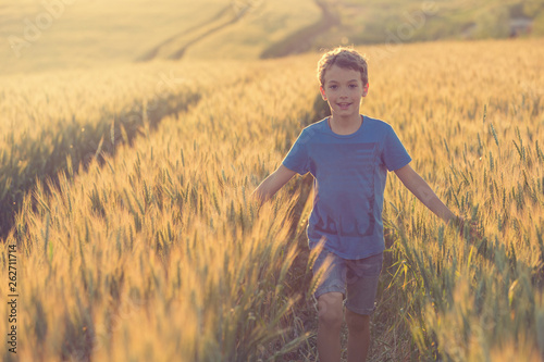 the boy, smiling, walks over the golden wheat field, spreading his arms to the sides, stroking the wheat, the concept of harvest photo