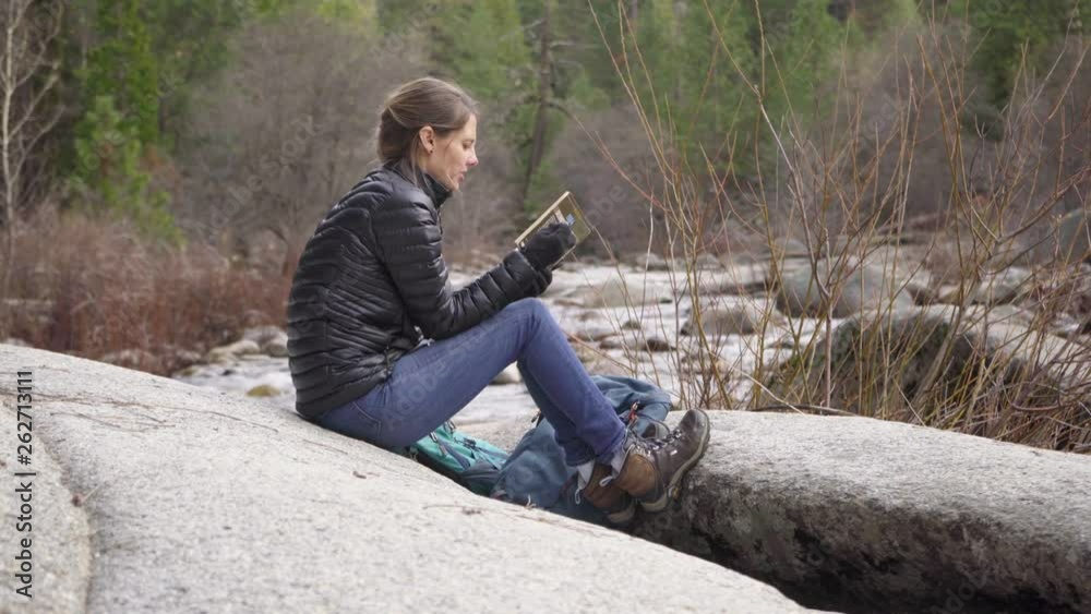 Beautiful woman reading on rock near a river after a hike Beautiful woman reading on rock near a river after a hike