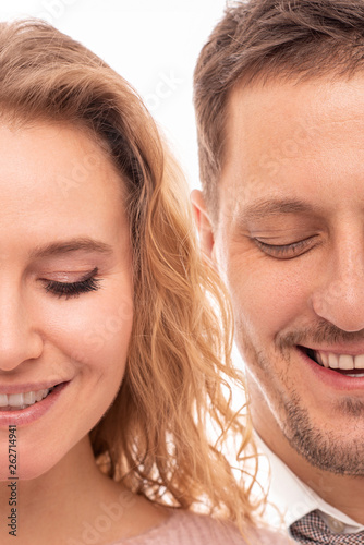 Close up portrait of two halves of a positive smiling man and woman with closed eyes on white background.  Halfface
