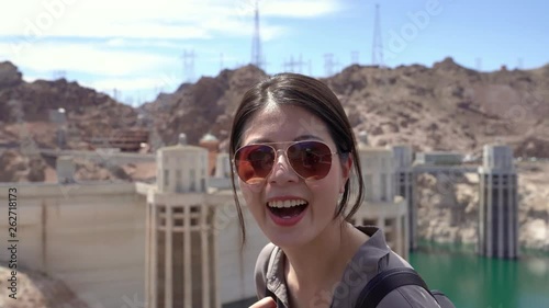 back view of young asian woman tourist hiking in nature mountain sightseeing Boulder Dam. cute girl turn head sending kiss face camera with blue sky in background. backpacker travel in usa lifestyle