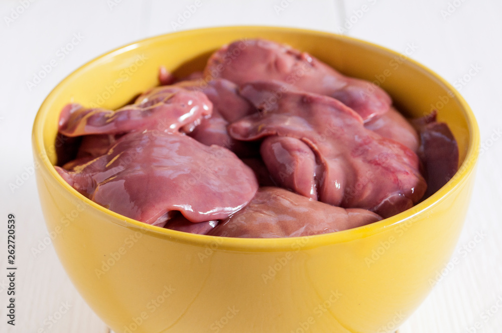 Raw chicken livers in a yellow bowl on a white wooden table. Close-up. Useful diet food. Raw chicken livers in a yellow bowl on a white wooden table. Close-up. Useful diet food.