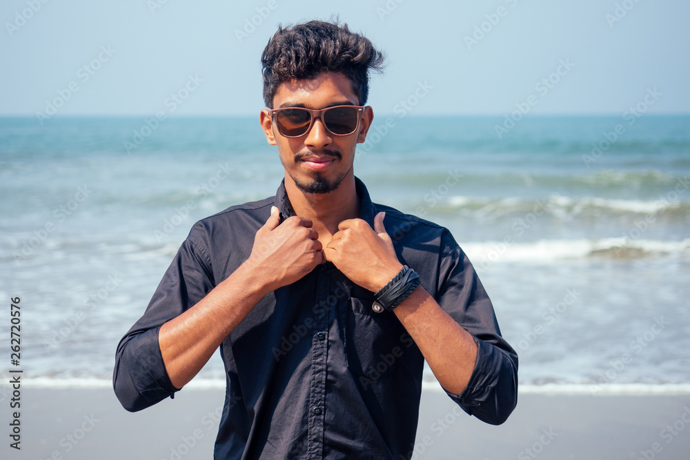 young hindu stylish man posing with sunglasses active beach vacation on semmertime happy Goa India beach. sunscreen spf protection concept.