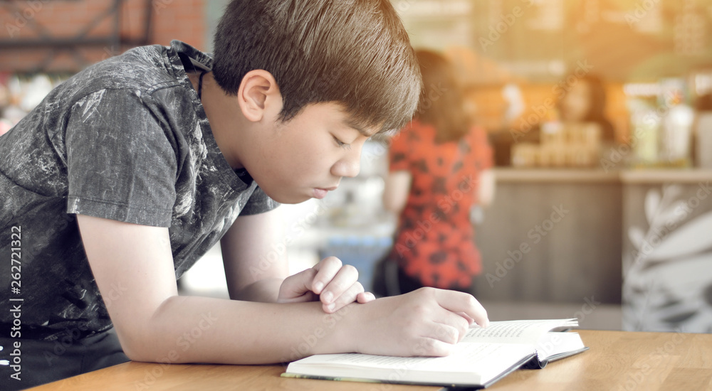 Asian cute boy read books while waiting for their mothers to buy drinks in the cafe.