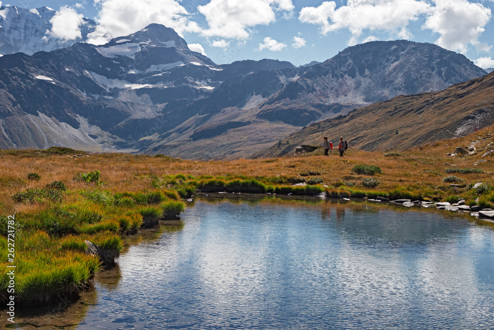 Some hikers near a pond with clear waters, on the mountains of the Simplon pass in Switzerland.