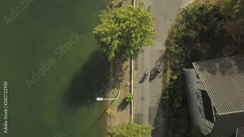 2 People drive with a bike along a river in Germany. We see cars and trees. photo