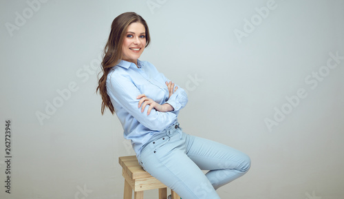 smiling young woman sits on stool with crossed arms.