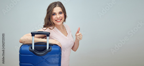 smiling woman with long hair standing with suitcase and doing thumb up.