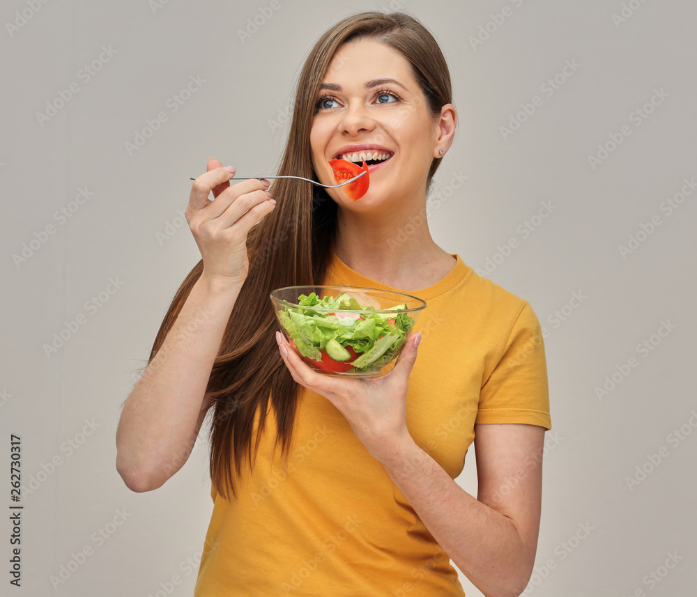 smiling woman eating vegetable salad from glass bowl.