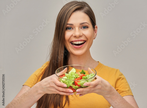 smiling woman holding glass bowl with green salad.