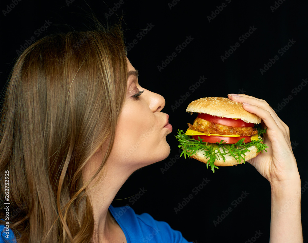 young woman biting burger on black background.